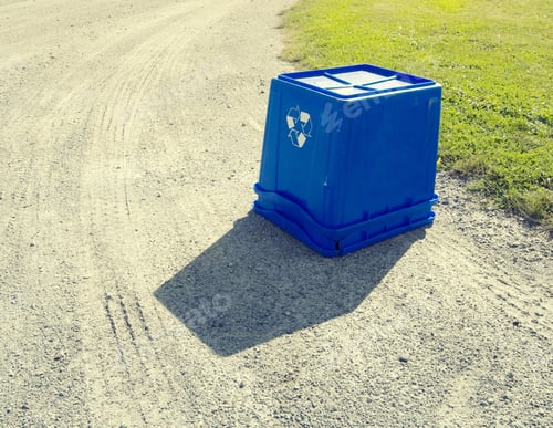 Preview: An Upside Down Blue Recycling Bin On A Gravel Road.