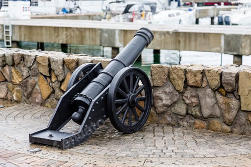 Preview: An Old Black, Iron Cannon At A Wall In A Marina
