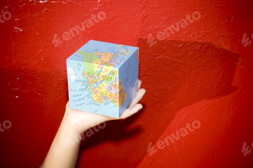 Preview: A Person Holding A Square Shaped Map In Front Of A Red Wall.