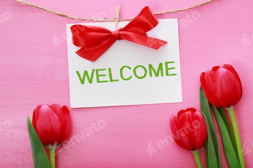 Preview: Inviting Welcome Card Hanging With Clothespins With Red Tulips On A Bright Pink Wood Background