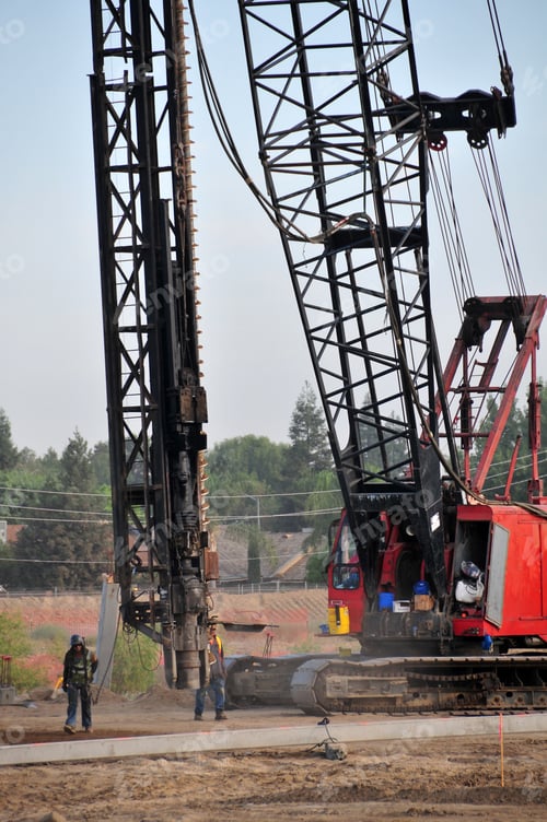 Preview: A Power Auger To Drill Deep Holes Is Supported By A Crane On A Construction Job Site