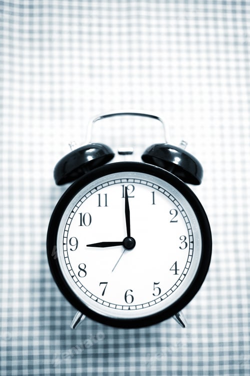 Preview: A Black Alarm Clock Sitting On A Checkered Table.