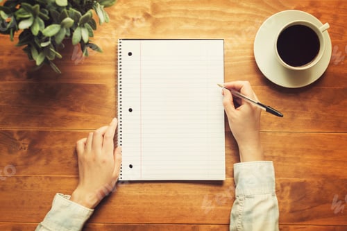 Preview: Hands Of A Person Writing In A Small Notepad On A Wooden Desk