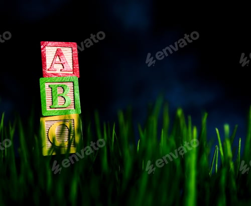 Preview: A Child'S Alphabet Blocks Stacked Outside In Green Grass.