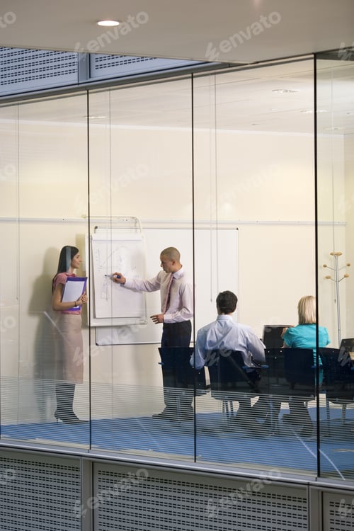 Preview: Business Couple Giving Presentation To Work Colleagues In Boardroom, Man Writing On Whiteboard