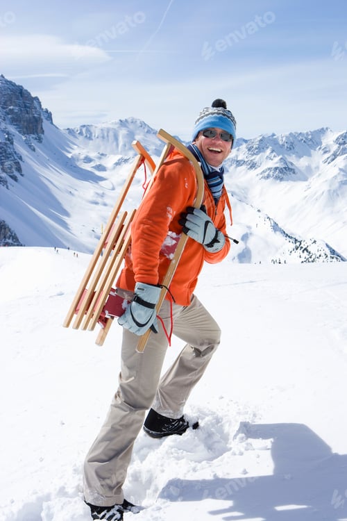 Preview: Man On Winter Vacation Walking In Snow Carrying A Sled Smiling At Camera