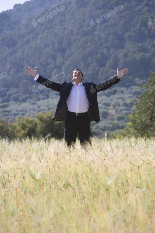 Preview: Happy Businessman Standing With Arms Outstretched In Rural Field
