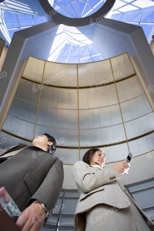 Preview: Businessman And Woman Standing Below Skylight In Airport, Woman Using Mobile Phone, Low Angle View