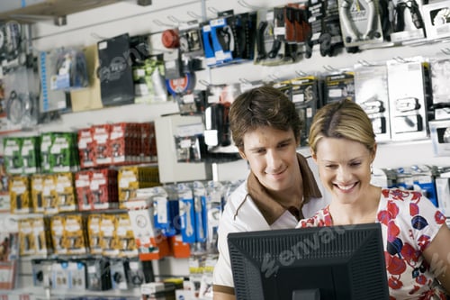 Preview: Young Couple Looking At Visual Screen Beside Bike Accessories Display Rack In Bicycle Shop, Smiling
