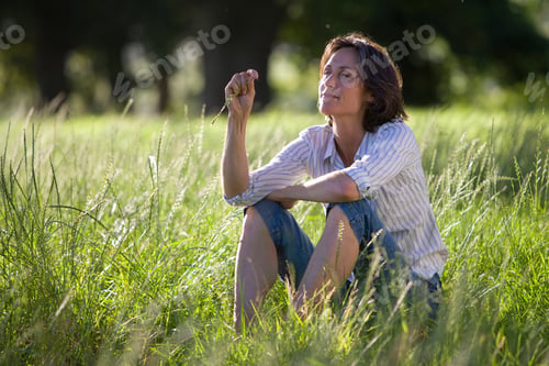 Preview: Thoughtful Mature Woman Sitting In Field Of Grass In Countryside