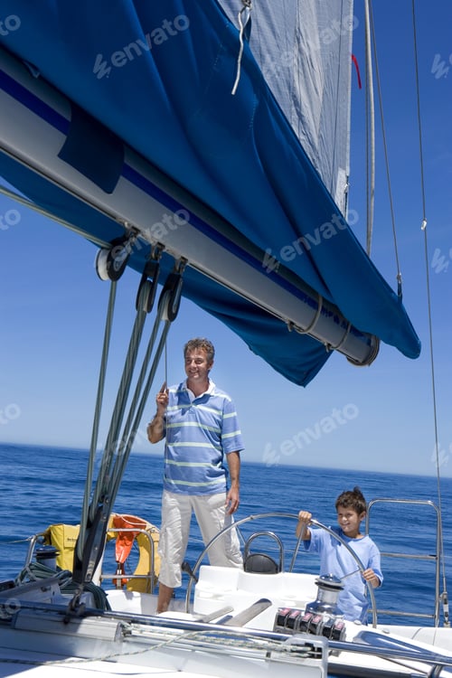 Preview: Father And Son (8-10) Standing At Helm Of Sailing Boat Out To Sea, Boy Steering, Man Holding