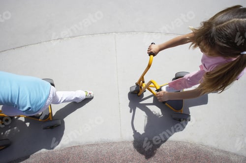 Preview: Two Girls (4-6) Riding Toy Push Scooters In Playground, Side View, Overhead View
