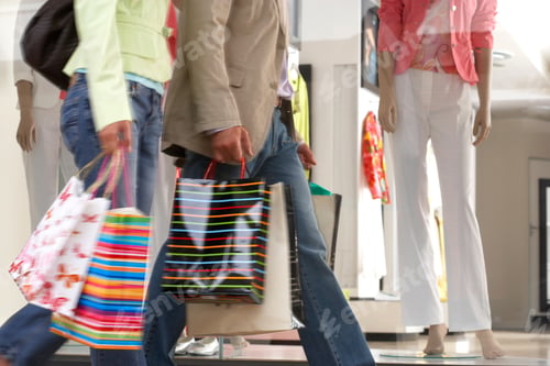 Preview: Couple With Shopping Bags Walking Past Clothes Fashion Shop Window In Retail Mall With Motion Blur