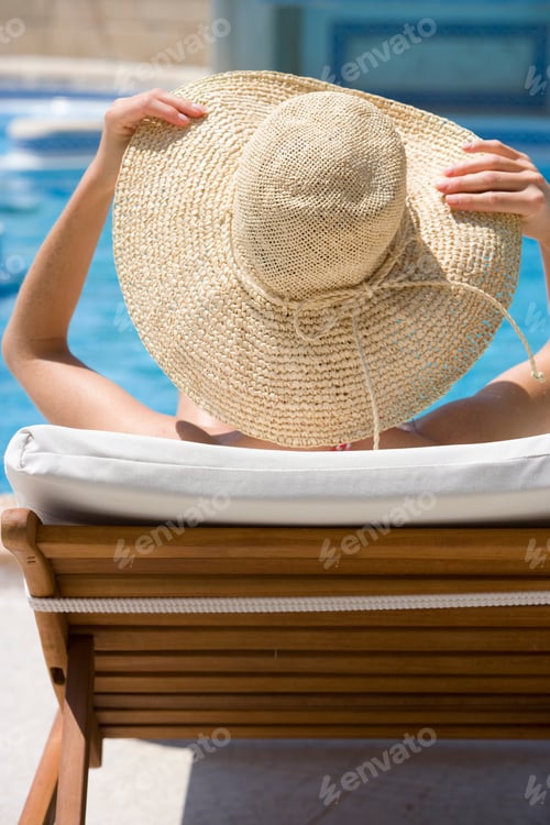 Preview: Woman On Holiday Wearing Sun Hat Relaxing On Lounger By Swimming Pool