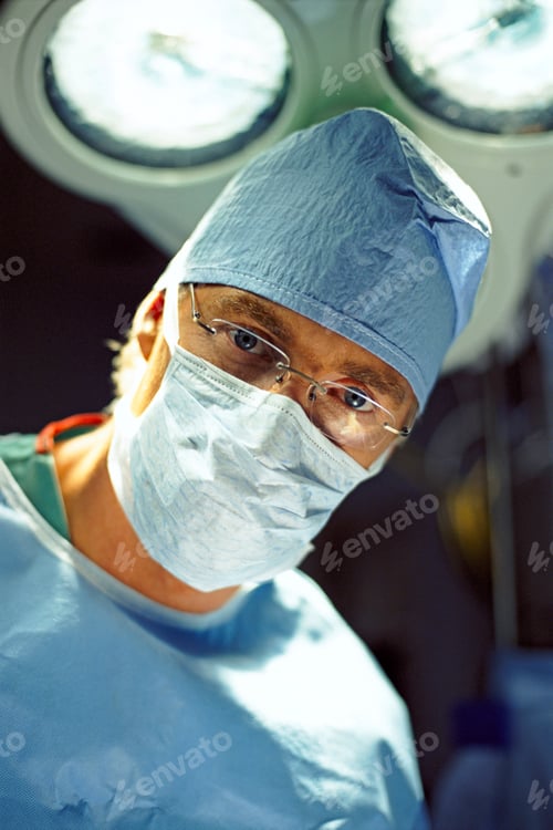 Preview: Surgeon In Mask And Scrubs In Hospital Operating Theatre Looking At Camera