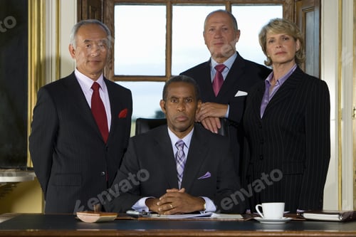Preview: Colleagues Standing Behind Mature Businessman At Desk With Paperwork, Portrait