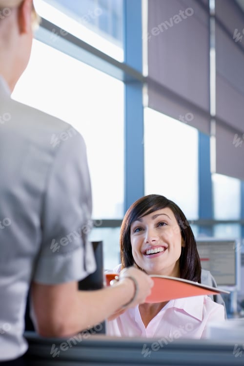 Preview: Businesswoman Handing Report To Smiling Co-Worker At Desk In Office
