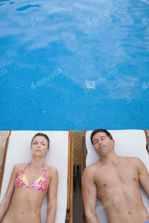 Preview: Couple Laying With Eyes Closed On Lounge Chairs At Poolside