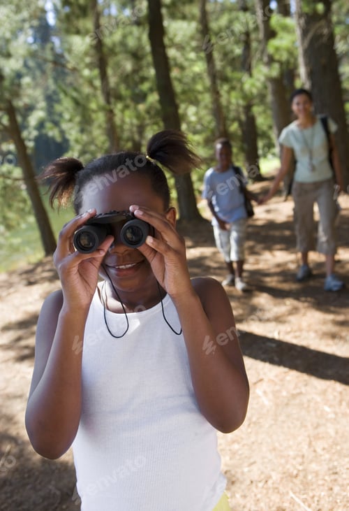 Preview: Family Hiking On Woodland Trail, Focus On Girl Looking Through Binoculars In Foreground