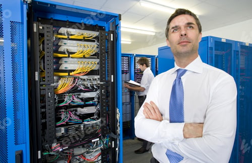 Preview: Businessman With Arms Crossed Looking Up Pensively In Network Server Room