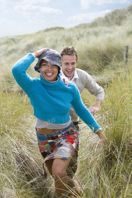 Preview: Young Happy Couple Running Through Grass At Beach