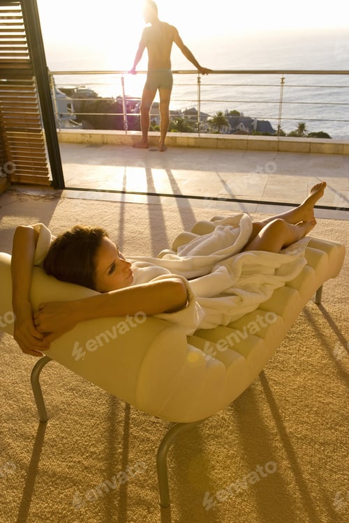 Preview: Young Woman Lying On Chaise Lounge, Man Standing On Balcony In Background