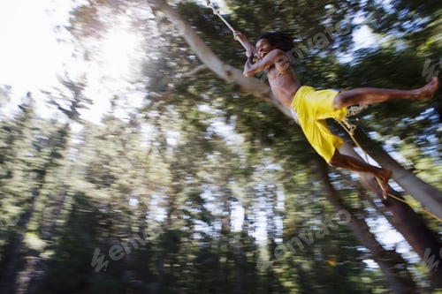 Preview: Boy (8-10), In Yellow Swimming Shorts, Swinging On Rope Above Lake, Low Angle View (Backlit)