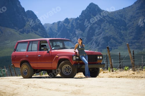 Preview: Young Woman Leaning Against Parked Red Suv On Dirt Track In Mountain Valley, Looking At Scenery