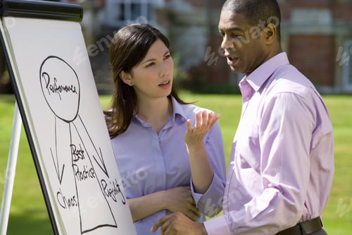 Preview: Young Businessman And Colleague Discussing Chart On Whiteboard Outdoors, Close-Up