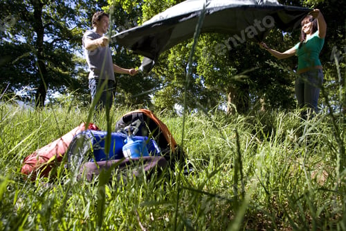 Preview: Young Couple Setting Up Tent On Camping Trip In Woodland Clearing, Side View (Surface Level)