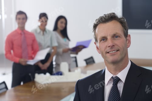 Preview: Businessman At Head Of Conference Table, Colleagues In Background, Smiling, Portrait