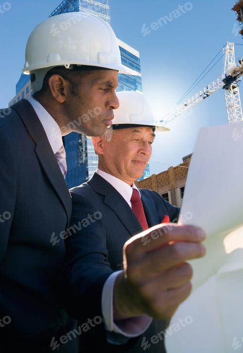 Preview: Businessmen In Hard Hats Meeting On Construction Site Looking At Plans