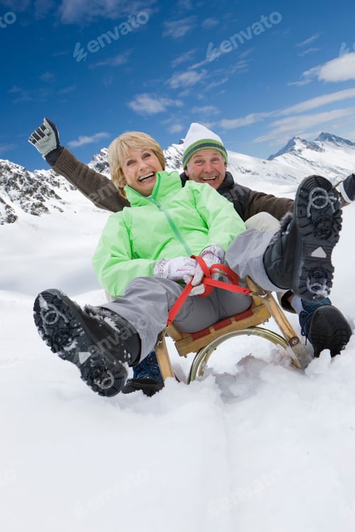 Preview: Senior Couple On Winter Vacation Riding On Sled Smiling At Camera