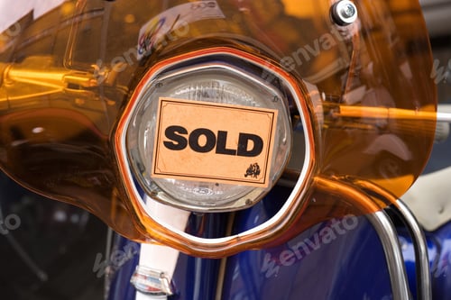 Preview: Orange Sold Sticker On Scooter Headlight In Shop, Close-Up, Front View