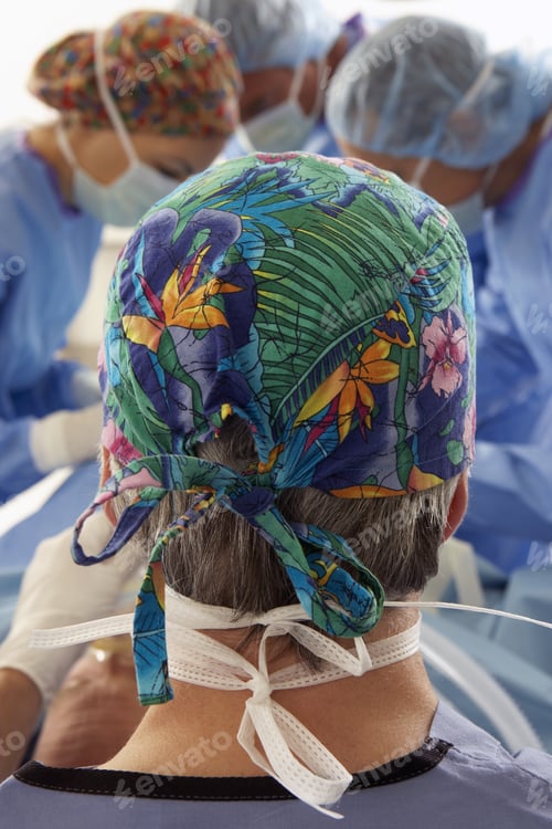 Preview: Surgeons In Scrubs Operating On Patient, Focus On Man In Foreground Wearing Bandana, Rear View