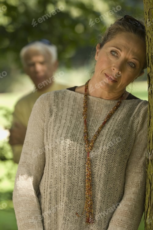Preview: A Woman Leaning On A Tree, Man Blurred In The Background.