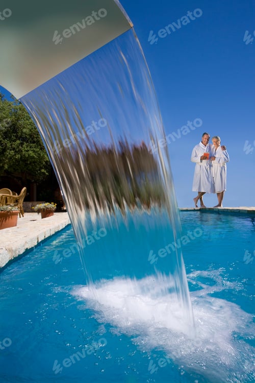 Preview: Couple In Bathrobes Standing At Edge Of Swimming Pool With Waterfall