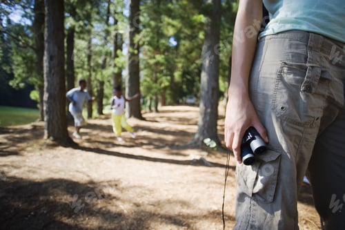 Preview: Family Hiking On Woodland Trail, Focus On Woman Holding Binoculars In Foreground, Mid-Section