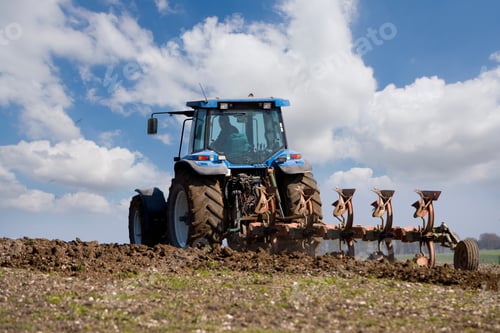 Preview: Farmer Ploughing Farm Field With Tractor Against Blue Sky