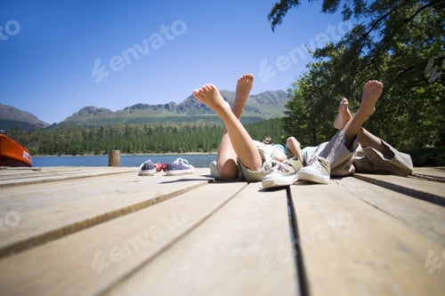 Preview: Boy And Girl (7-10) Lying Side By Side On Lake Jetty, Shoes Off, Rear View (Surface Level)