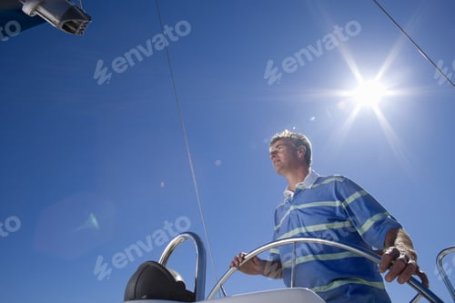 Preview: Man In Striped Blue Polo Shirt Standing At Helm Of Sailing Boat Out At Sea, Steering, Low Angle