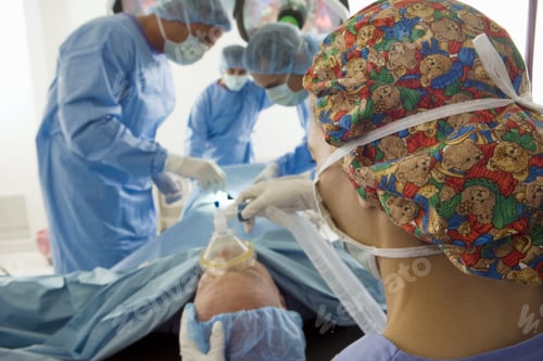 Preview: Surgeons Operating On Patient, Focus On Man Holding Oxygen Mask In Foreground, Rear View