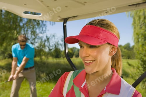 Preview: Close-Up Of A Mid Adult Woman Smiling In A Golf Cart With A Mid Adult Man Playing Golf In The
