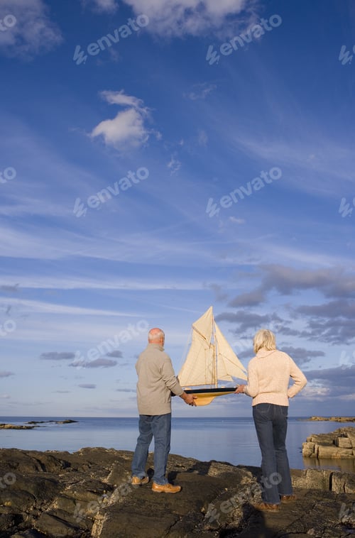 Preview: Senior Couple With Model Boat On Rocks By Sea, Rear View
