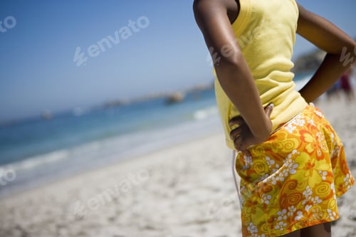 Preview: Girl In Yellow Vest And Shorts Standing On Beach, Hands On Hips, Rear View, Mid-Section (Tilt)