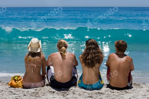 Preview: Four Teenagers Sitting On Beach Looking At Sea Waves On Summer Vacation