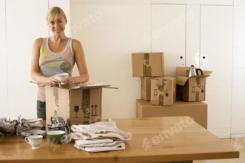 Preview: Woman Moving House, Packing Crockery Wrapped In Paper In Box On Dining Room Table, Smiling, Portrait