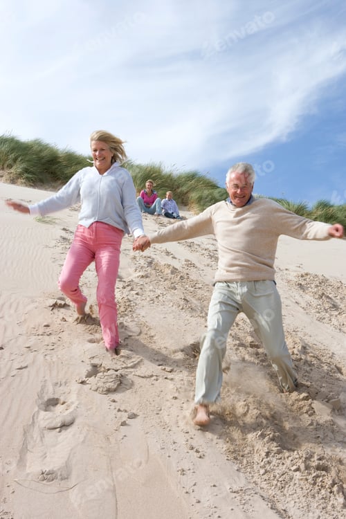 Preview: Active Grandparents Running Down Sand Dune On Beach Holding Hands