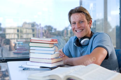 Preview: Smiling Male Student Studying In Library Wearing Headphone At Camera