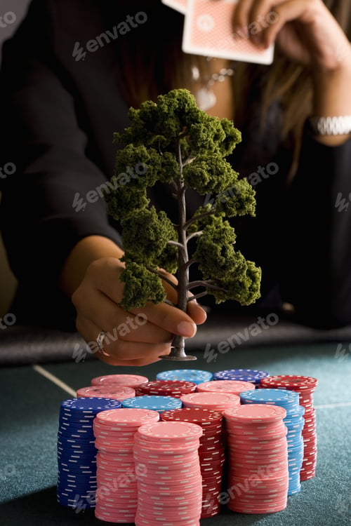 Preview: Woman Placing Model Tree On Pile Of Gambling Chips On Table, Mid Section